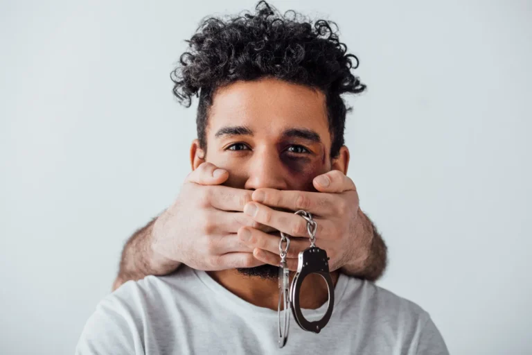 A male hands covering a mans mouth with handcuffs hanging.