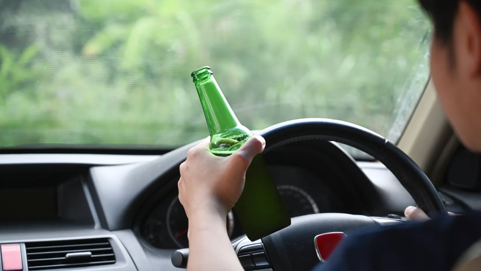 Driver holding a beer bottle while driving, representing a situation often leading to DUI bail bonds.