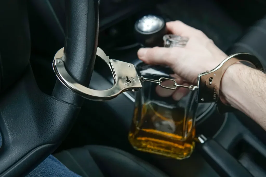 A man inside his car with a handcuff and a bottle of alcohol drink.